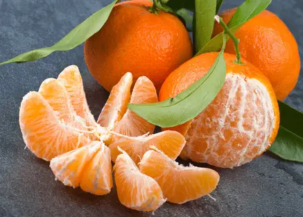three tangerines with one peeled and sliced tangerine